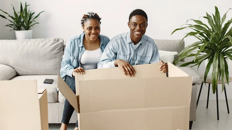 Smiling couple seated with an open cardboard moving box