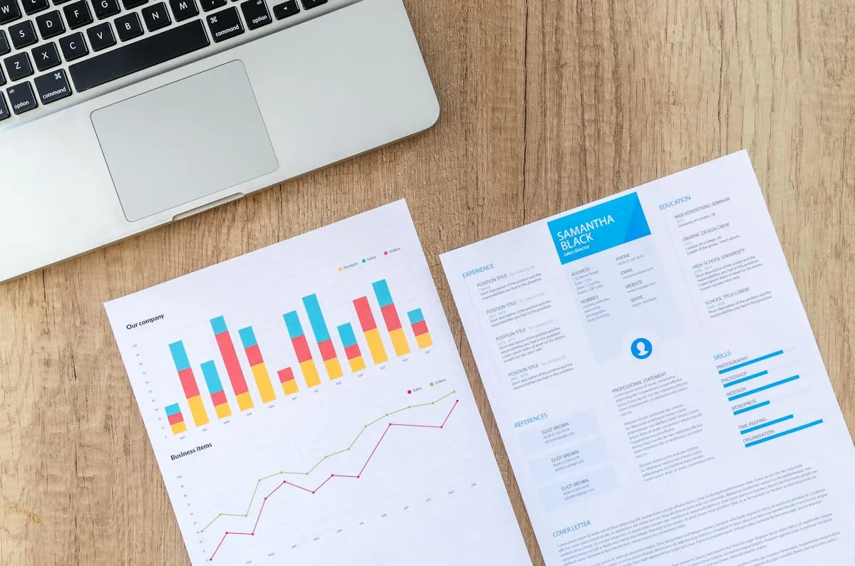 Resume and business performance charts on a desk next to a laptop
